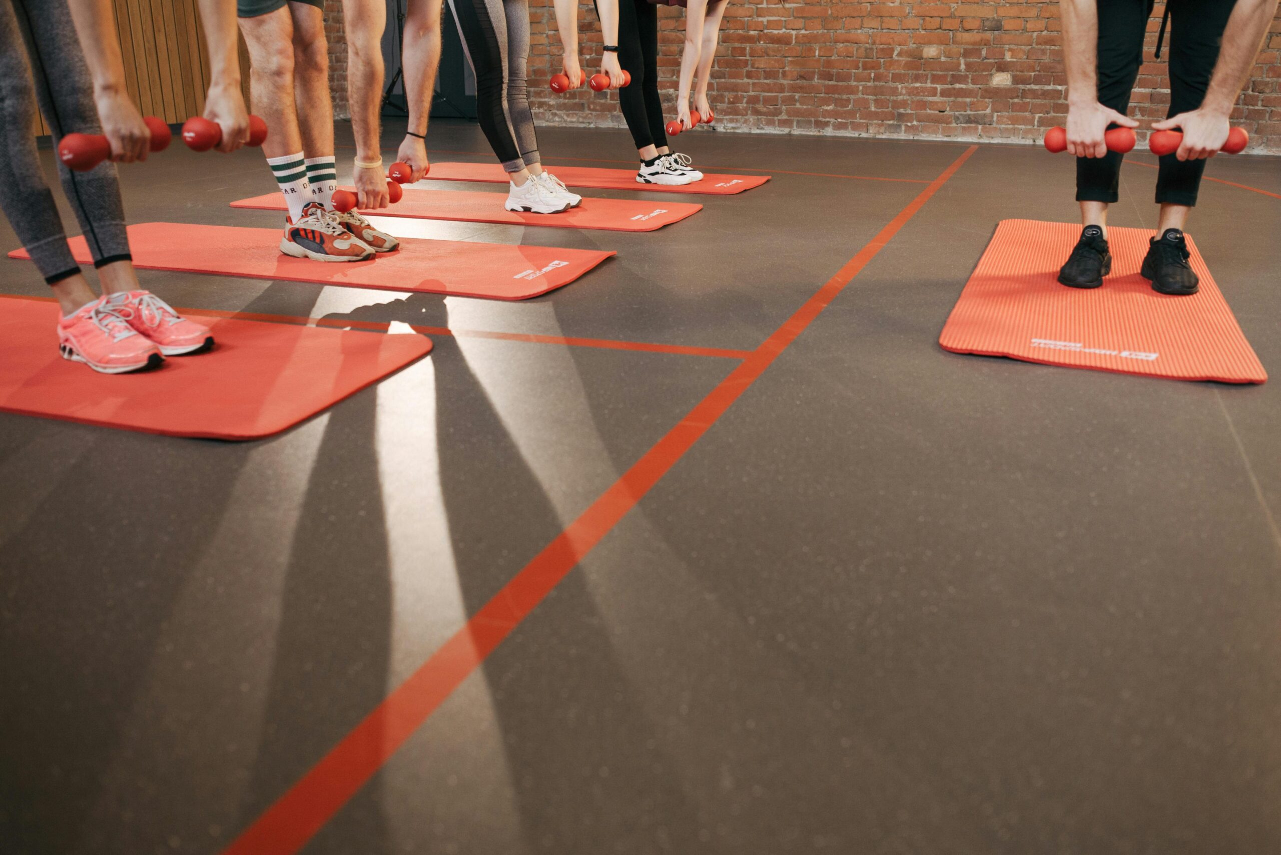 A group workout session with dumbbells on red yoga mats indoors, focusing on fitness and health.