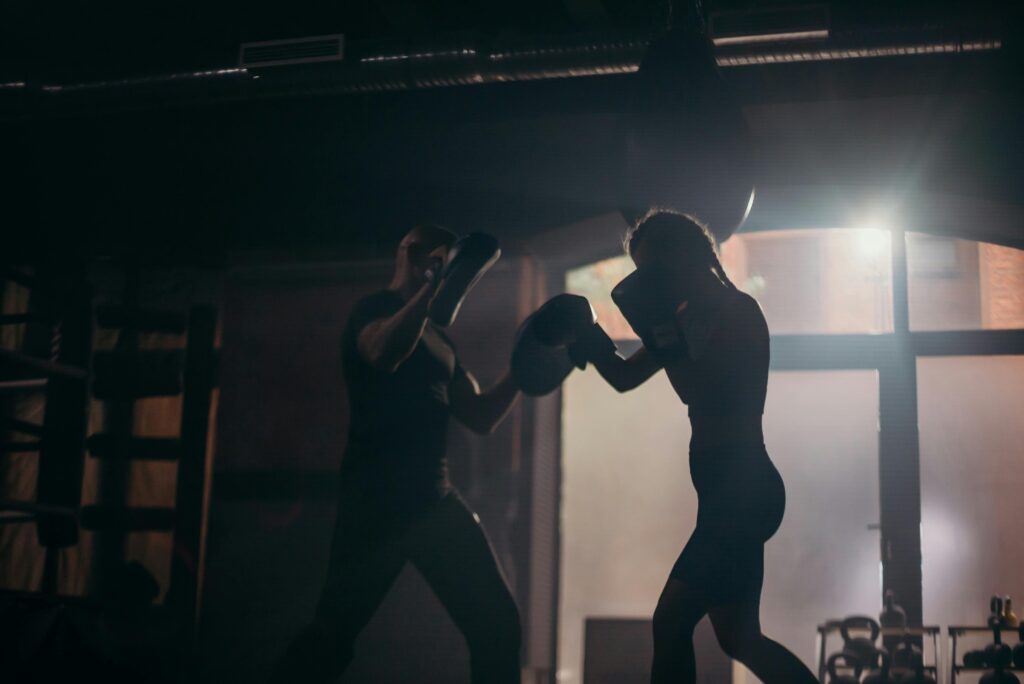 Silhouetted boxers sparring during an intense training session in a dimly lit gym.