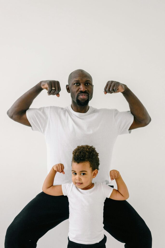 African American father and son flexing muscles against white backdrop